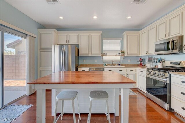 kitchen with wooden counters, a kitchen island, a sink, stainless steel appliances, and dark wood-type flooring