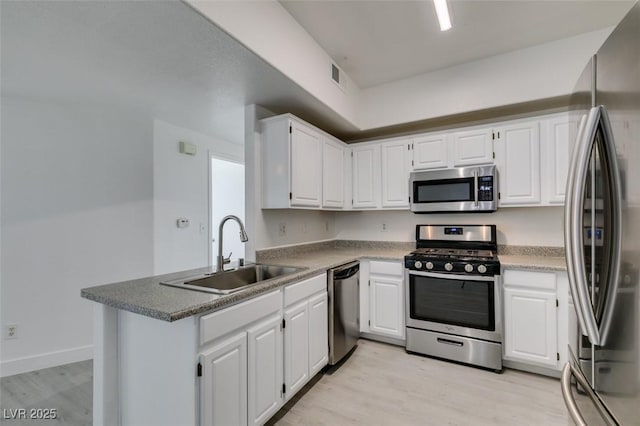 kitchen featuring a sink, stainless steel appliances, light wood-type flooring, and a peninsula