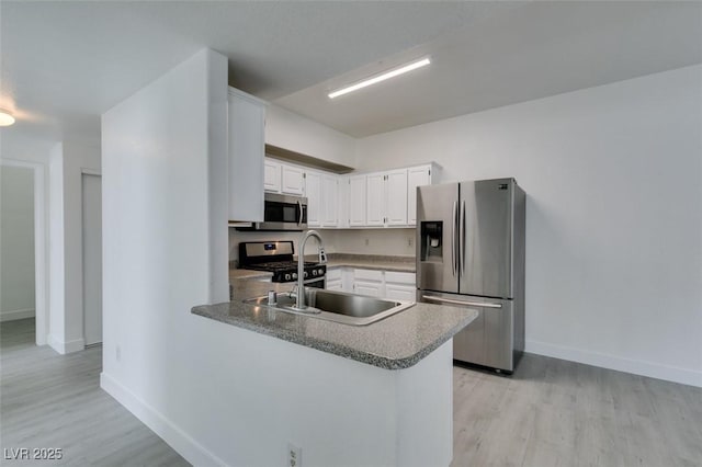 kitchen with a peninsula, light wood-style flooring, a sink, stainless steel appliances, and white cabinets