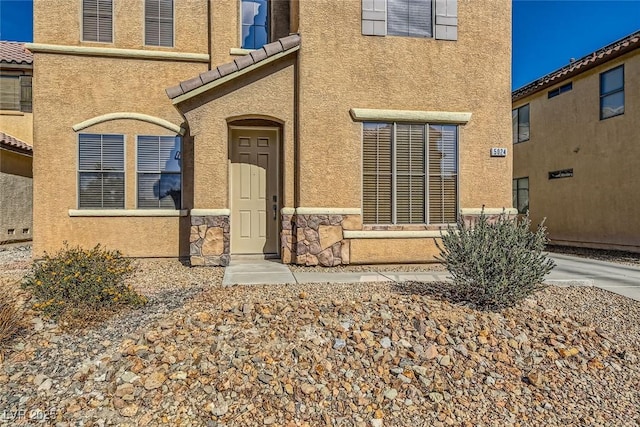 view of exterior entry featuring stone siding, stucco siding, and a tile roof