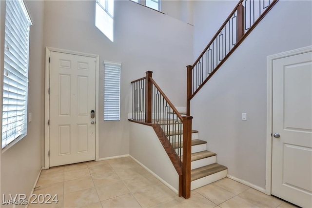 foyer featuring light tile patterned flooring, baseboards, and a towering ceiling