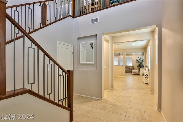 foyer entrance featuring baseboards, visible vents, light tile patterned flooring, stairs, and a towering ceiling