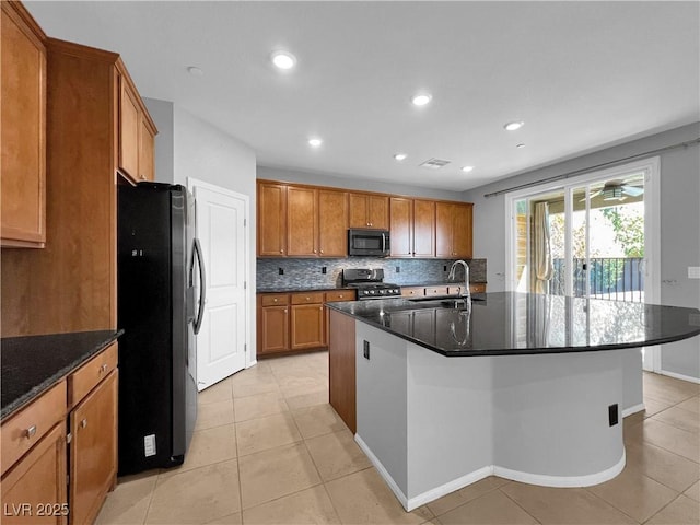 kitchen featuring stainless steel gas range oven, backsplash, freestanding refrigerator, brown cabinetry, and a sink