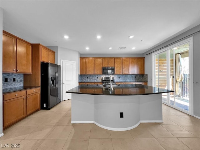 kitchen featuring brown cabinets, black fridge, stainless steel microwave, dark countertops, and stove