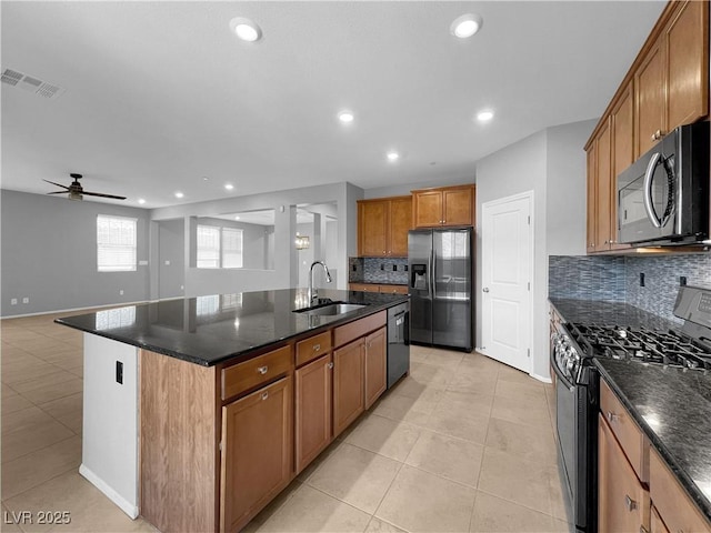 kitchen with a center island with sink, light tile patterned floors, brown cabinetry, black appliances, and a sink