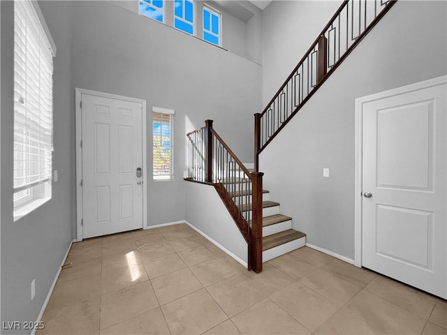 foyer entrance with light tile patterned flooring, stairs, baseboards, and a towering ceiling