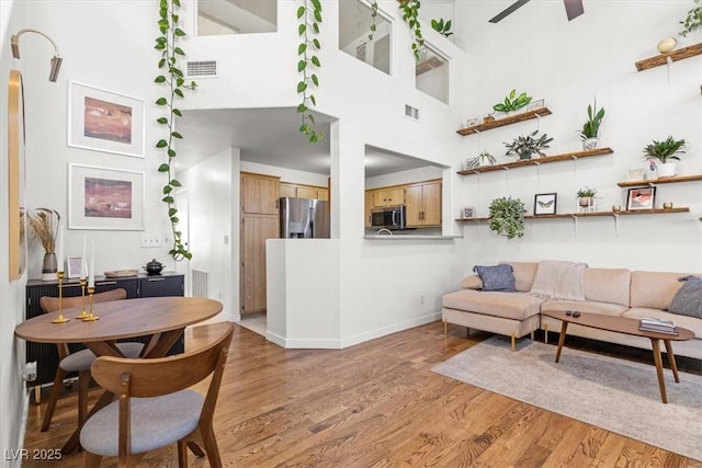 living room with light wood-type flooring, visible vents, ceiling fan, and a towering ceiling