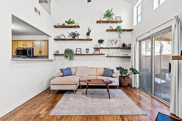 living area featuring wood finished floors, visible vents, a towering ceiling, and baseboards