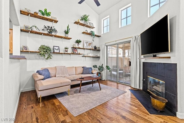 living room featuring wood finished floors, baseboards, high vaulted ceiling, a fireplace, and ceiling fan