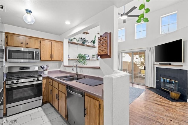 kitchen featuring a tiled fireplace, a sink, open shelves, open floor plan, and appliances with stainless steel finishes