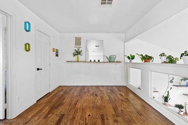 interior space with vaulted ceiling, wood finished floors, visible vents, and baseboards