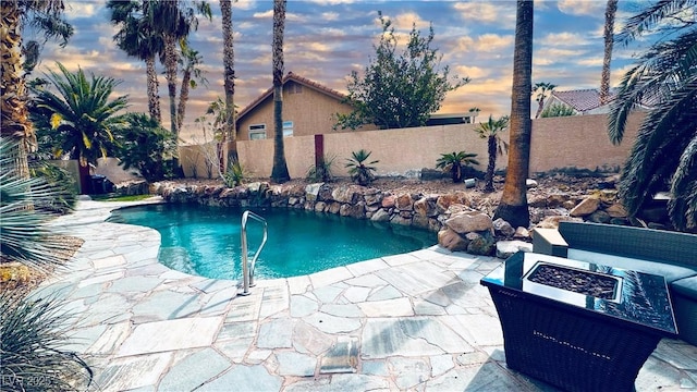 pool at dusk with a fenced in pool, a fire pit, a fenced backyard, and a patio area