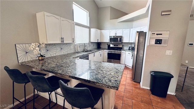 kitchen featuring a sink, tasteful backsplash, stainless steel appliances, a peninsula, and white cabinets