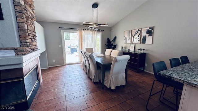 dining space with an inviting chandelier, a fireplace, baseboards, and vaulted ceiling