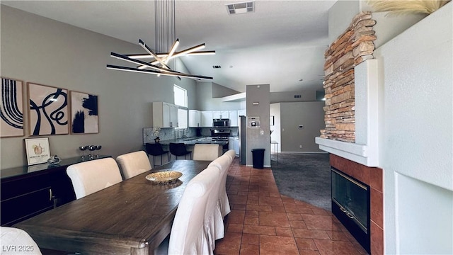 dining space featuring visible vents, high vaulted ceiling, stone finish floor, a stone fireplace, and an inviting chandelier