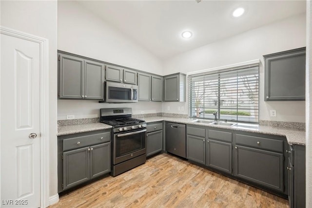 kitchen featuring light wood-type flooring, gray cabinets, a sink, appliances with stainless steel finishes, and vaulted ceiling