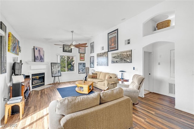 living room with arched walkways, a fireplace with flush hearth, visible vents, and wood finished floors