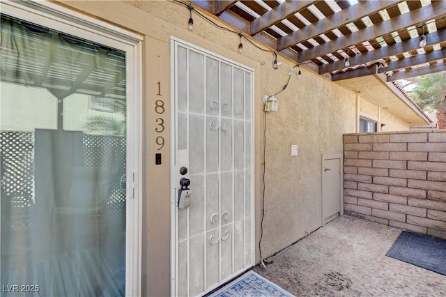 entrance to property featuring fence, a pergola, and stucco siding