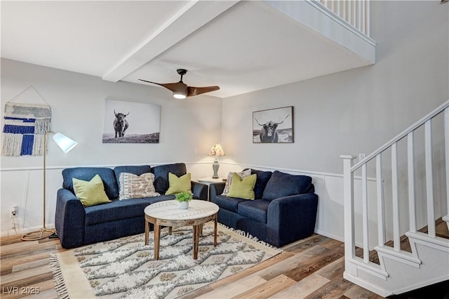 living room with a ceiling fan, stairway, wood finished floors, and beamed ceiling