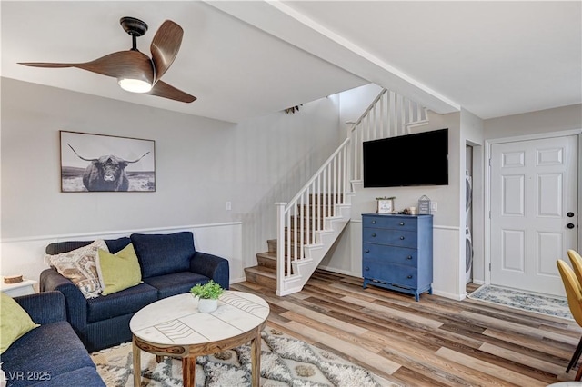 living area featuring stairs, light wood-style floors, and a ceiling fan