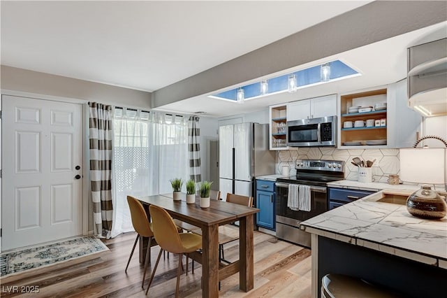 kitchen with open shelves, light wood-style flooring, appliances with stainless steel finishes, blue cabinets, and a sink