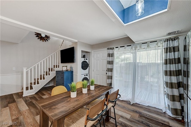 dining area with visible vents, stairs, a skylight, wood finished floors, and stacked washer / drying machine