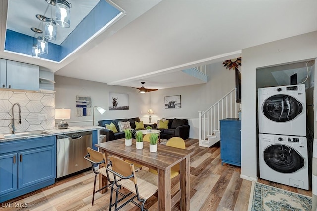 kitchen with light wood-style flooring, a sink, blue cabinetry, stacked washer / drying machine, and dishwasher