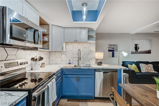 kitchen featuring blue cabinetry, open shelves, tile countertops, appliances with stainless steel finishes, and a sink