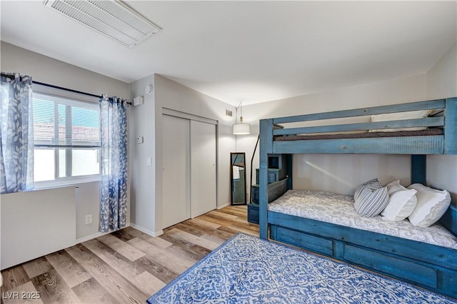 bedroom with baseboards, visible vents, light wood-style flooring, elevator, and a closet