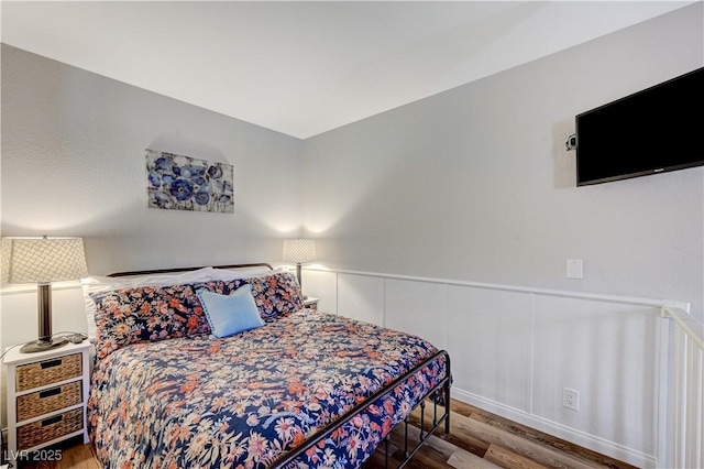 bedroom featuring a wainscoted wall, wood finished floors, and a decorative wall