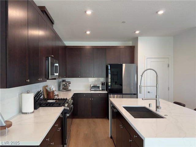 kitchen with a kitchen island with sink, dark brown cabinets, appliances with stainless steel finishes, and a sink