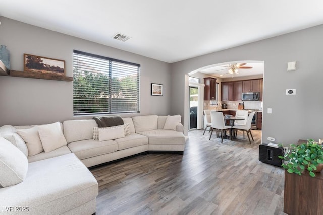 living room featuring visible vents, arched walkways, light wood-style floors, and a ceiling fan