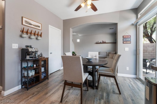 dining area featuring ceiling fan, baseboards, arched walkways, and wood finished floors