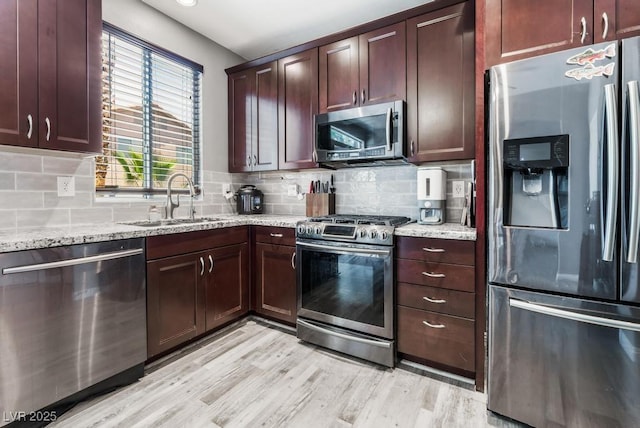 kitchen featuring light stone counters, light wood-style flooring, a sink, appliances with stainless steel finishes, and tasteful backsplash