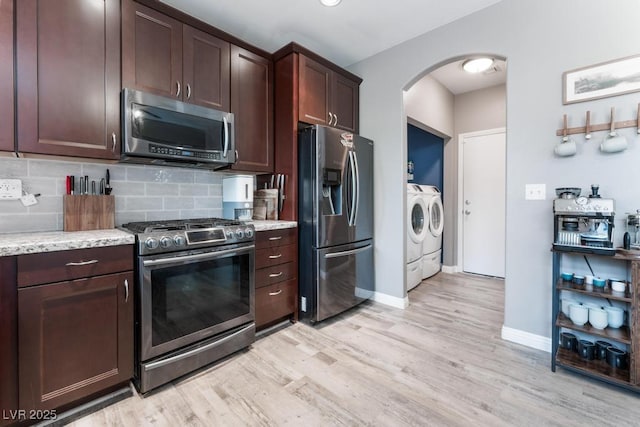 kitchen featuring light wood-type flooring, washer and dryer, stainless steel appliances, arched walkways, and decorative backsplash