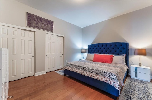 bedroom featuring wood finished floors, baseboards, and two closets