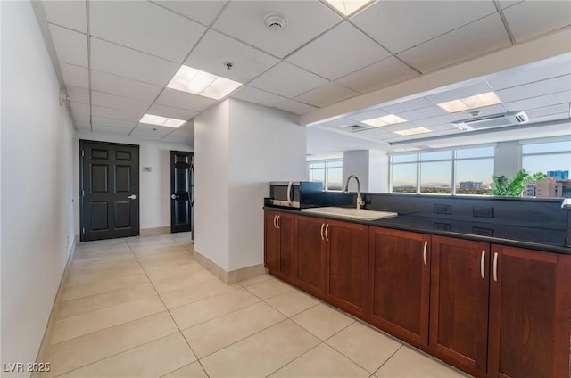 kitchen featuring light tile patterned floors, dark countertops, a sink, a paneled ceiling, and stainless steel microwave