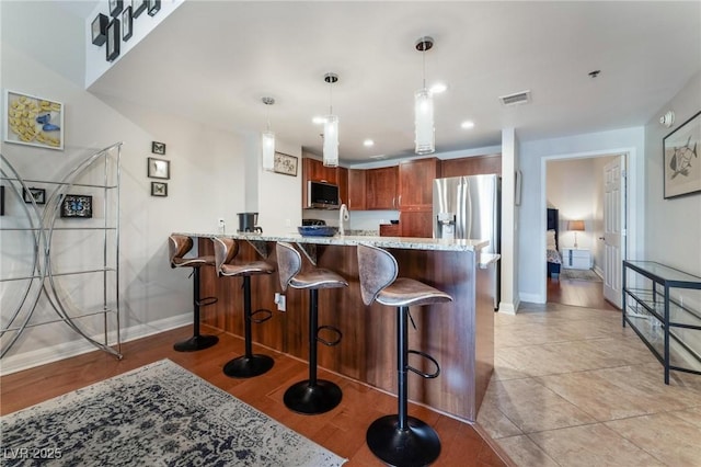 kitchen featuring a kitchen bar, pendant lighting, stainless steel appliances, a peninsula, and light stone countertops