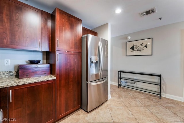 kitchen with visible vents, light stone counters, stainless steel fridge with ice dispenser, light tile patterned floors, and baseboards