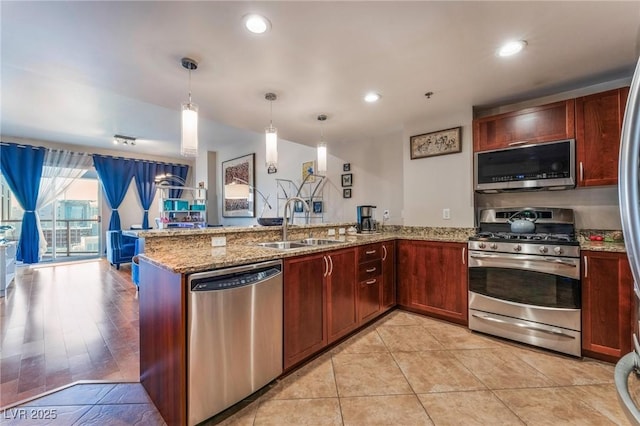 kitchen featuring light stone countertops, a peninsula, a sink, appliances with stainless steel finishes, and decorative light fixtures