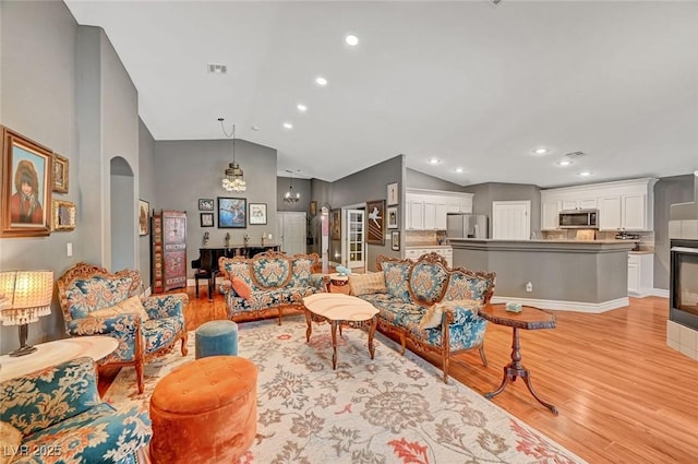 living room featuring light wood-type flooring, arched walkways, visible vents, and vaulted ceiling