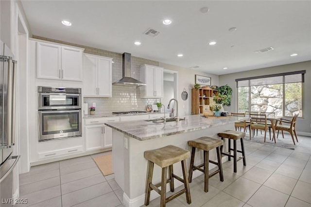 kitchen featuring visible vents, a sink, stainless steel appliances, wall chimney exhaust hood, and light tile patterned floors