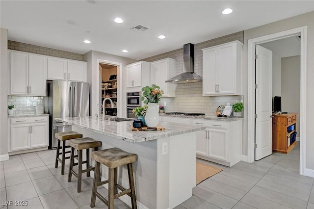 kitchen with a kitchen bar, a sink, white cabinetry, stainless steel appliances, and wall chimney range hood