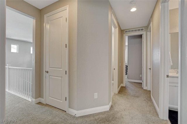 hall with visible vents, baseboards, and light colored carpet