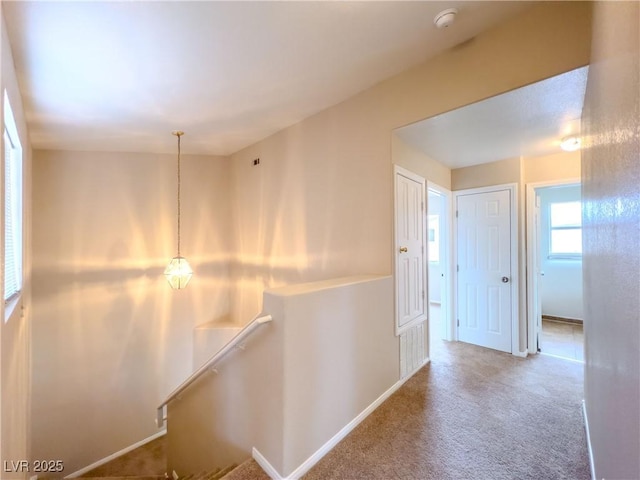 hallway with carpet flooring, an upstairs landing, and baseboards