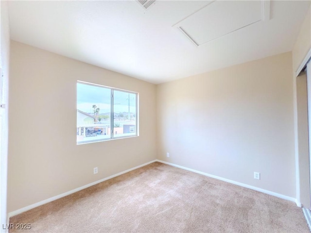 carpeted spare room featuring attic access and baseboards