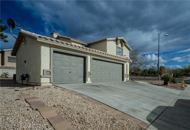 view of side of property featuring stucco siding, concrete driveway, an attached garage, and a tiled roof