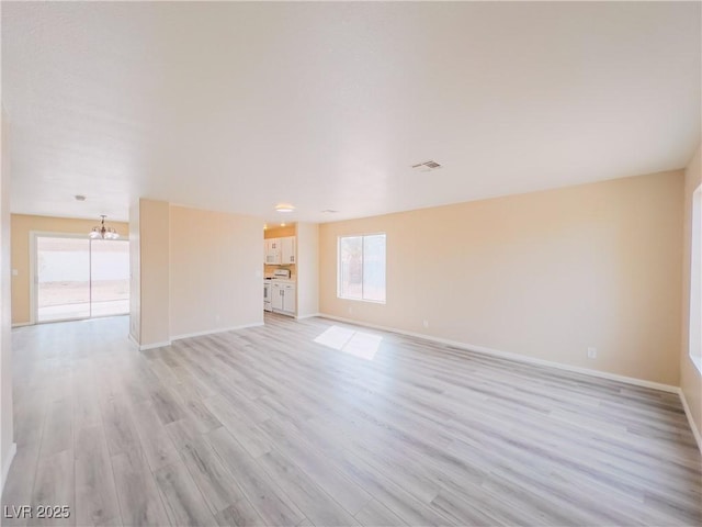 unfurnished living room with light wood finished floors, baseboards, and an inviting chandelier