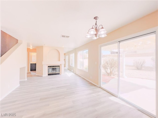 unfurnished living room with a tiled fireplace, light wood-style flooring, baseboards, and visible vents