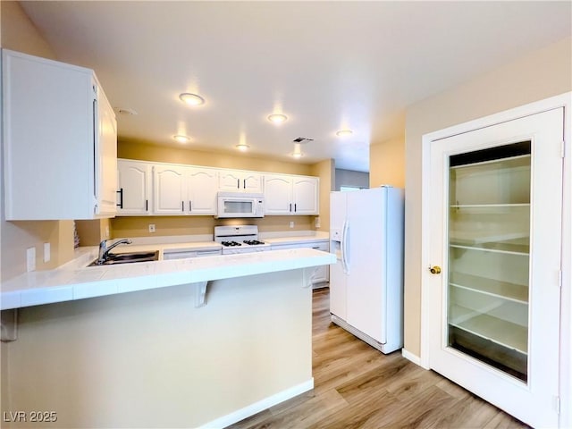 kitchen featuring tile counters, a peninsula, light wood-style floors, white appliances, and a sink